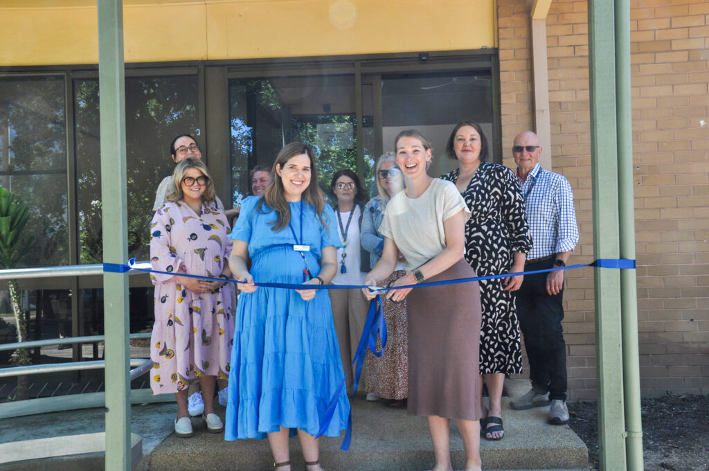 Group of people looking happy, cutting ribbon to open building