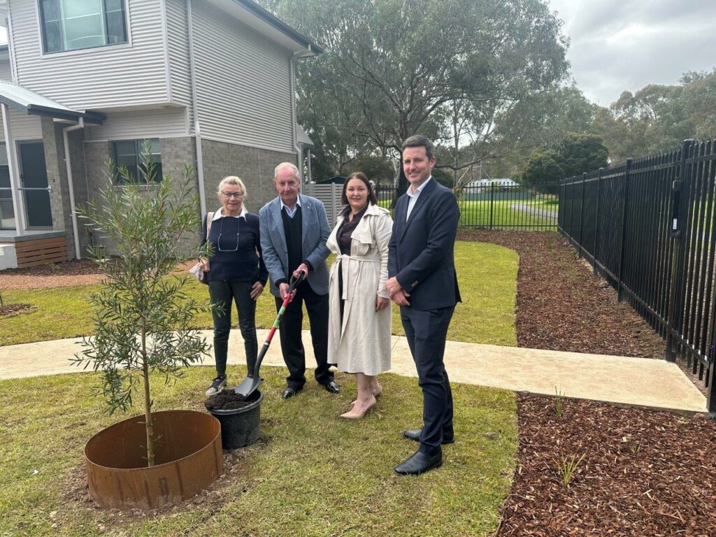 Four adults standing around newly planted tree