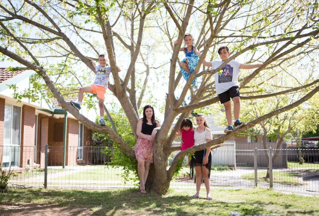 family standing around a tree with children climbing the branches