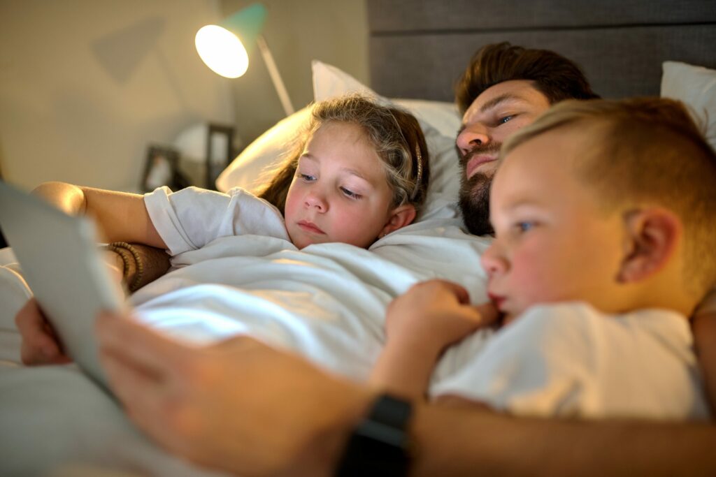 family of man and two children reading a book in bed