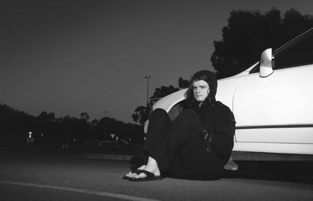 man sitting on ground and leaning against a car