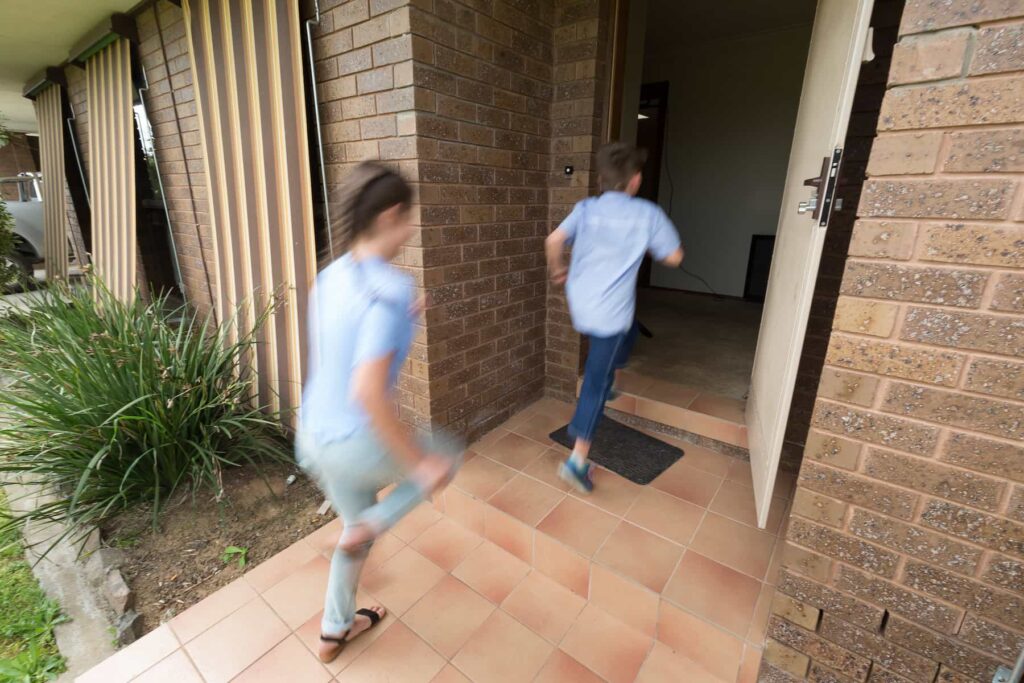 two children running toward the front door of a home