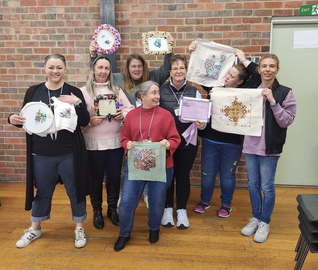 Group of women standing, showcasing their stitching work