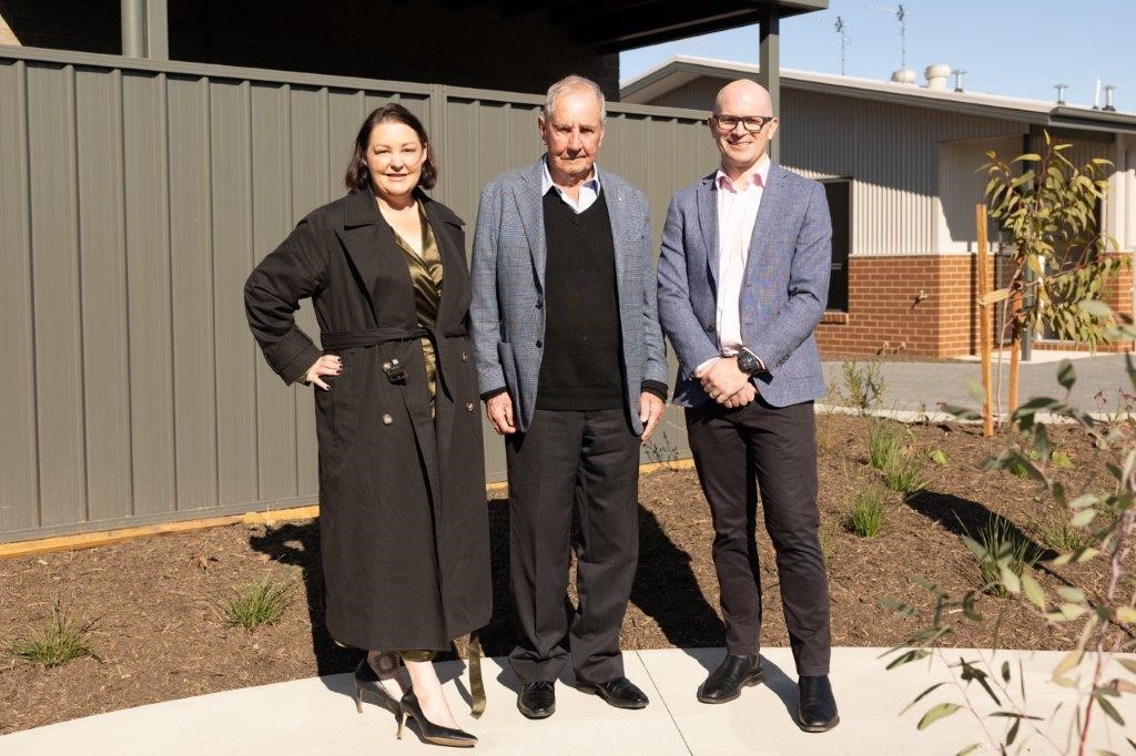 Three people standing in the sun in front of a garden